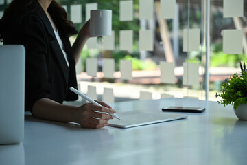 Close-up image of businesswoman hand using a stylus pen and digital tablet with graphic charts on...
