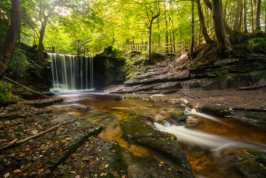 Epic beautiful Autumn landscape image of Nant Mill waterfall in Wales with glowing sunlight through the woodland