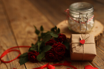 Naklejka na ściany i meble A gift in craft paper on a wooden background, red roses around, a jar of marshmallows, a letter in an envelope and hearts. Picture for Valentine's Day. The concept of gifts and lovers. High-quality ph