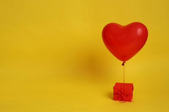 A heart-shaped balloon is tied to a red gift on a yellow background. Picture for Valentine's Day. The concept of gifts and lovers. High-quality photography