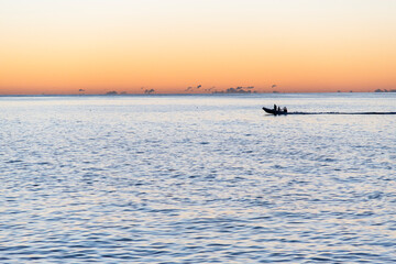 Fototapeta premium Small boat crossing the horizon at sunrise