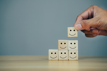 Closeup hands holding smiley face icon on wooden cube, service rating, leadership and corporate hierarchy concept.