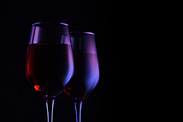 Two wine glasses on a dark background with neon highlights. Creative party concept.