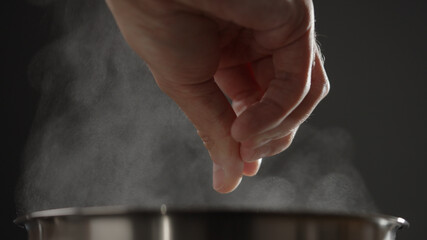 man adding salt to boiling water in saucepan with strong backlight