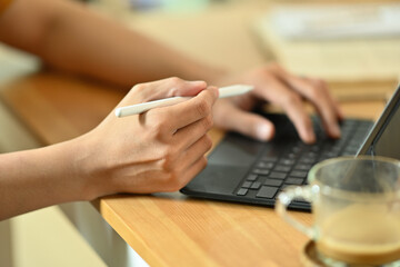 Cropped image of a young freelance man using a digital tablet and stylus pen at the wooden working...