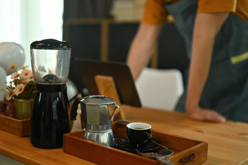 Photo of barista's hand using a digital tablet at the wooden counter surrounded by coffee equipment.