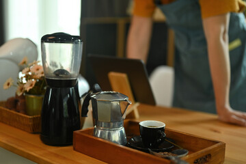 Photo of barista's hand using a digital tablet at the wooden counter surrounded by coffee equipment.