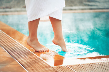 A girl puts her foot in a pool with hot thermal water, a wellness vacation at hot springs. - Powered by Adobe