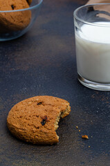 morning breakfast with a half-eaten cookie with a glass of milk on a dark table and a cup of chocolate cookies.
