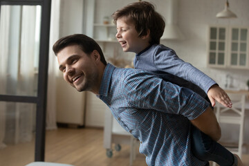 Loving Caucasian father piggy backing laughing little son, smiling caring young Caucasian dad...