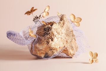 stone in mesh bag with dry flowers on beige background. art, stylish concept. beauty of nature and plastic in photography.concept of nature protection