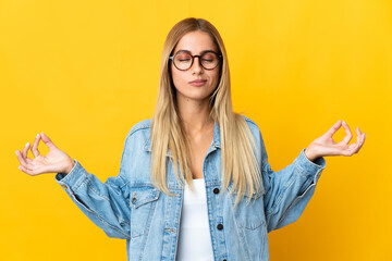 Young blonde woman isolated on yellow background in zen pose