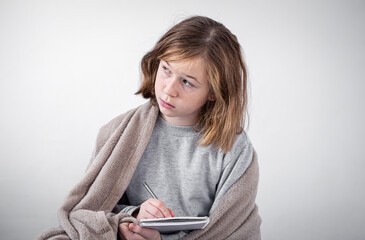 Little girl draws in a notebook, wrapped in a plaid on a white background.