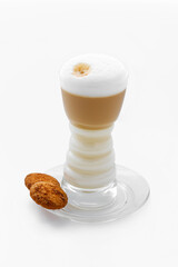 Serving coffee - a tall transparent cup with cappuccino coffee, white fluffy foam at the top, on a saucer, two small brown cookies. Isolated