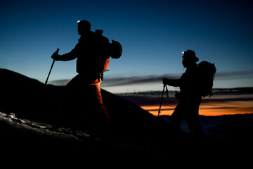 Close-up view of silhouettes of skiers climbing the mountain against the backdrop of evening sky