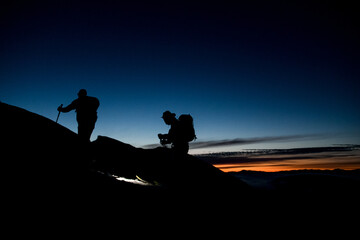 Fototapeta na wymiar dark silhouettes of skiers climbing the mountain against the backdrop of evening sky