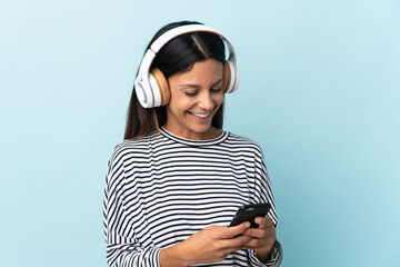 Caucasian girl isolated on blue background listening music and looking to mobile