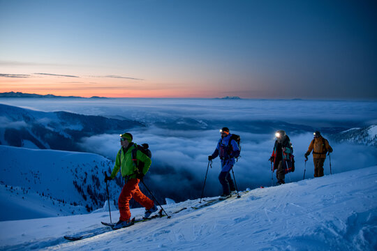 group of skiers with flashlights walking along mountain slope against the backdrop of picturesque evening sky