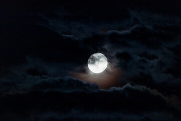 full moon with dark clouds in front of it in the night sky