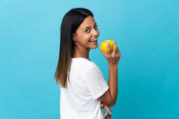 Caucasian girl isolated on blue background eating an apple