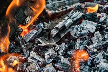 Glowing embers in hot red color, abstract background. The hot embers of burning wood log fire. Firewood burning on grill. Texture fire bonfire embers.