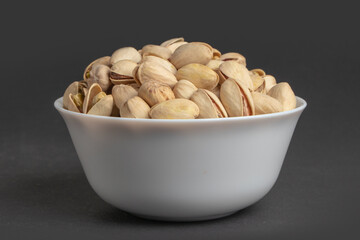 White bowl of pistachios on dark background
