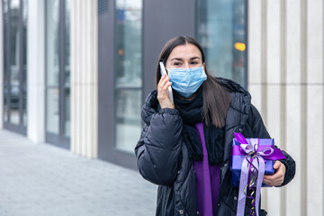 Young woman in a protective mask with a gift in his hands talking on the phone.