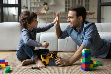 Happy father and little son giving high five, repairing toy car with screwdriver, playing on floor...