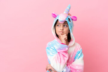 Little caucasian woman wearing a unicorn pajama isolated on pink background looking to the side and smiling