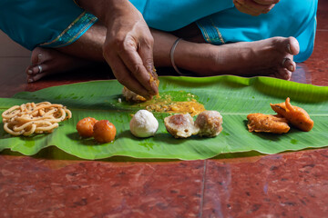 Woman eating traditional food served on banana leaf on Indian festival day.
