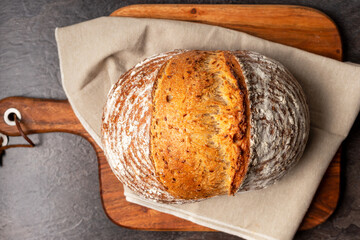 Wholemeal sourdough bread on linen napkin on brown wooden chopping board.