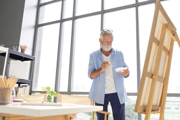 Fototapeta premium senior man painting a picture from paintbrush in free time