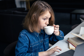 Tired girl in front of a laptop with a cup of tea and books.
