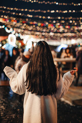 Young brunette woman in white long winter fur coat at the Christmas market with golden magic lights