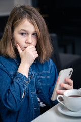 A teenager girl looks surprised at the smartphone screen.