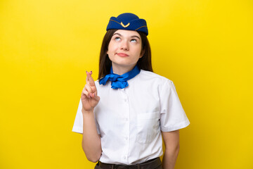 Airplane stewardess Russian woman isolated on yellow background with fingers crossing and wishing the best