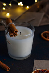 A white extinguished candle on a dark background with dried oranges and cinnamon sticks with spices for mulled wine. And Christmas lights.