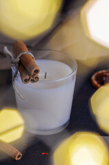 A white extinguished candle on a dark background with dried oranges and cinnamon sticks with spices for mulled wine. And Christmas lights.