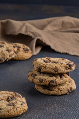 Sweet oatmeal cookies with pieces of chocolate on a dark table in the form of a stack and with a brown napkin.