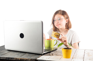 The girl is holding a bank card. Girl near computer with a credit card. Online shopping. Shop...