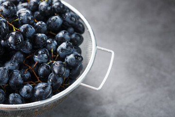 Sweet black grapes in a metal bowl on a dark textured background.