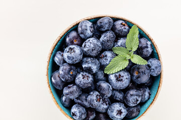 Ripe blueberries with water drops in a bowl on a pastel background,