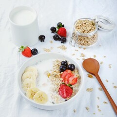 bowl of granola with yogurt, strawberry and berries on a white cloth-lined table. Healthy breakfast, top view. Dishes suitable for diet, healthy lifestyle.