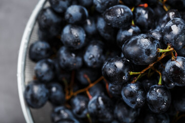Sweet black grapes in a metal bowl on a dark textured background.