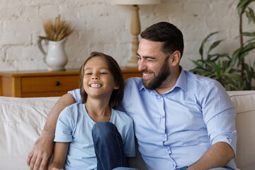 Happy bonding caring young father cuddling small preteen child son, enjoying spending time together communicating at home, joking having fun, friendly two male generations family relations concept.