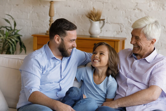 Joyful Friendly Young Man Talking Joking With Laughing Small Preteen Kid Son And Old Senior Retired Father, Having Fun Resting On Sofa At Home, Happy Three Male Generations Family Relations Concept.