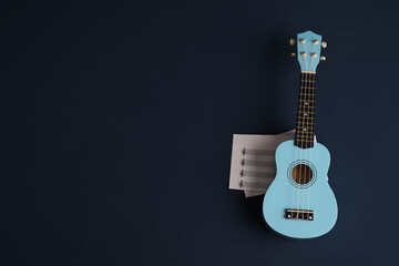 A small blue ukulele guitar with a sheet music on a blue background. The concept of a music store or education. High-quality photography
