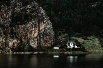 Scenic landscape of nature of Norway. Houses on the shore of the fjord. Huge rock and green trees.
