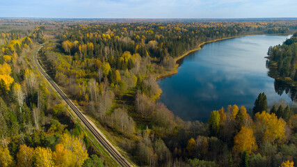 A beautiful view from above of the autumn forest and lake, the view from the drone. The railway passes through the forest.