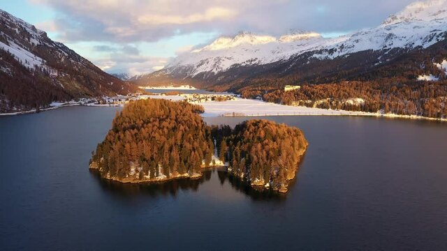 Aerial drone footage of the sunset over the Silsersee lake in winter in the Engadine valley in Sils Maria village in Canton Graubunden in the Swiss alps. Shot with a forward and rotation motion